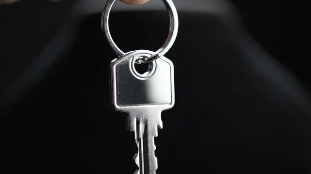 Close-up of a silver key attached to a round keyring against a dark blurred background