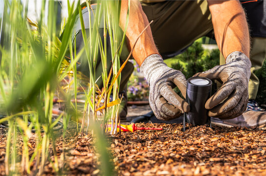 Worker installing a garden spotlight in a mulched flower bed