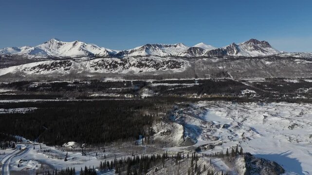 Panoramic Drone Shot Revealing Rugged Mountain Peaks Above Snowy Wilderness