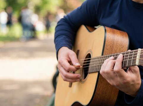 Close up of hands playing an acoustic guitar outdoors. Musician strumming strings with a pick in a sunny park