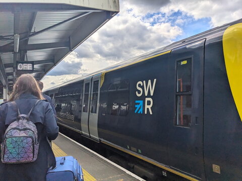 Passengers with luggage waiting next to a South Western Railway train at New Malden railway station