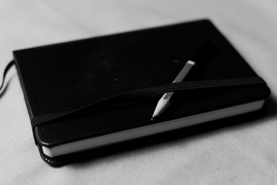 Greyscale photograph of a sketchbook with a drawing pencil on top. 