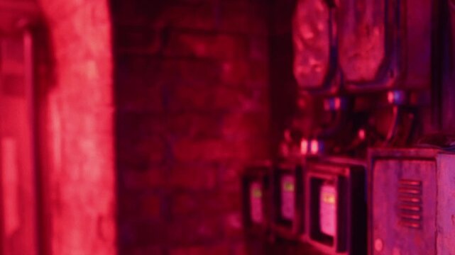 Bright red lights fill an industrial area with electrical meters and equipment. The setting has brick walls, creating a unique atmosphere. The focus is on modern technology in use.