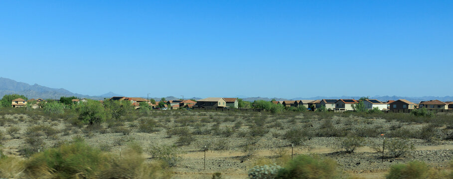 Desert residential neighborhood houses situated behind an arid desert landscape under a clear blue sky, Buckeye, Arizona
