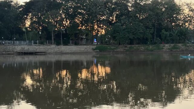 Trees reflecting on calm Ping river with kayaks at sunset in Chiang Mai