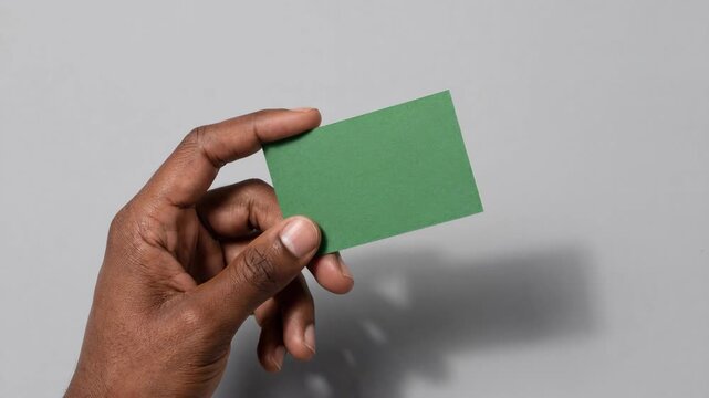dark skinned hand holding a blank green rectangular card against a plain light grey background with soft shadow