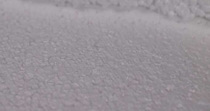A sheet of foam with an uneven fracture, white foam demonstrates a structure of small balls of polystyrene in place of the torn edge of the material.