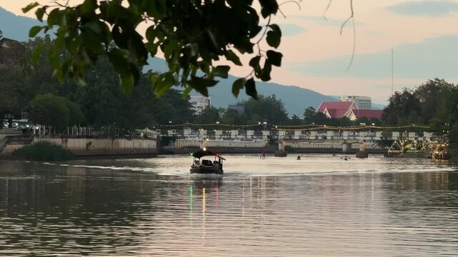 Boat cruising on Ping river with bridge at sunset in Chiang Mai
