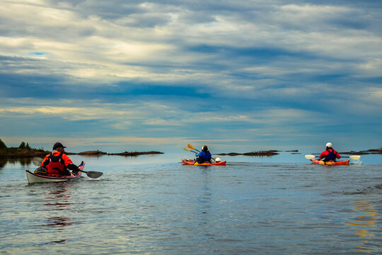 Sea kayakers heading out toward an open horizon under a dramatic cloudy sky on a calm morning, copy space and room for text, Georgian Bay, Ontario