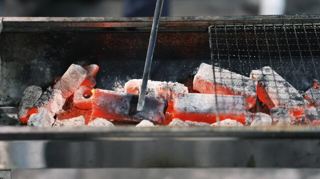 Glowing charcoal briquettes in grill with metal grate and poker