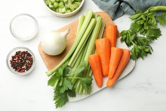Fresh celery stalks, carrots, onion bulb and spices on white table, flat lay