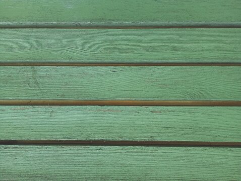 A detailed full-frame texture of old weathered horizontal wooden planks painted in a rustic green color, showcasing a natural timber grain pattern, parallel rows, and a cracked surface.