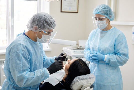 Dentist and Assistant in Protective Gear Examining Female Patient Teeth in Modern Dental Clinic Office