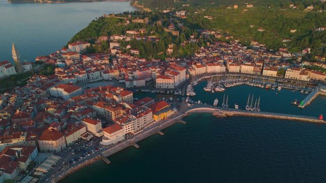 Cinematic aerial drone orbit over Piran harbor revealing Tartini Square and St. George's Parish Church at sunset, Slovenia.