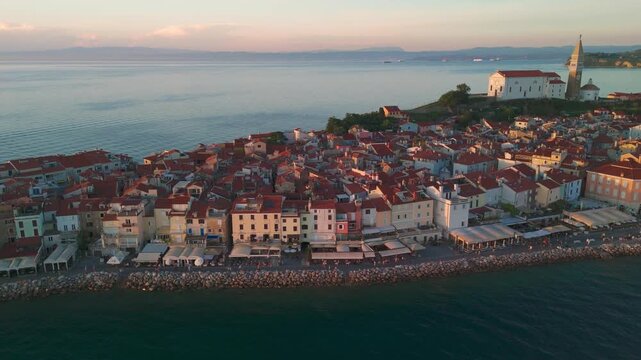 Cinematic aerial view of Piran old town waterfront at sunset, drone flying sideways from right to left.
