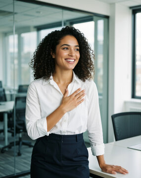 A hopeful young African-American woman stands in a bright office, hand on heart, touched by a kind word, exuding grateful vitality.