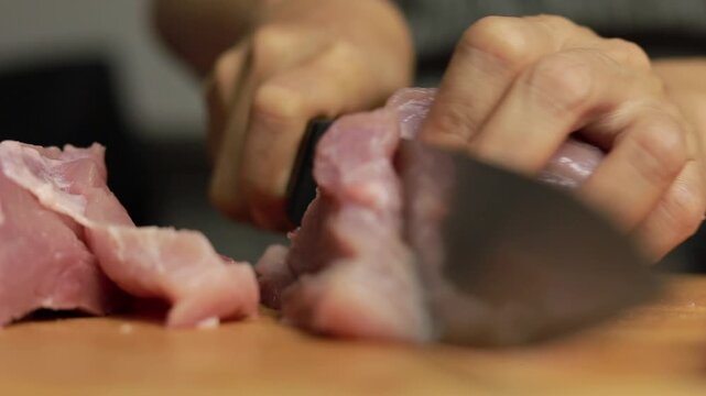 Hands slicing raw pork meat on a cutting board