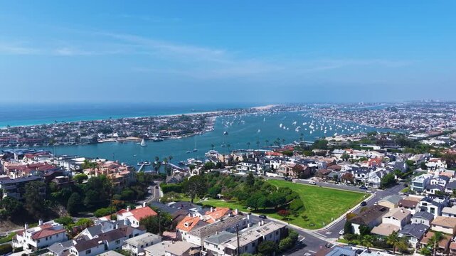 Aerial sweep across the horizon in Newport Beach California reveals Newport Bay and the Pacific Ocean under a Blue West Coast Sky with the city of Corona Del Mar in the foreground.