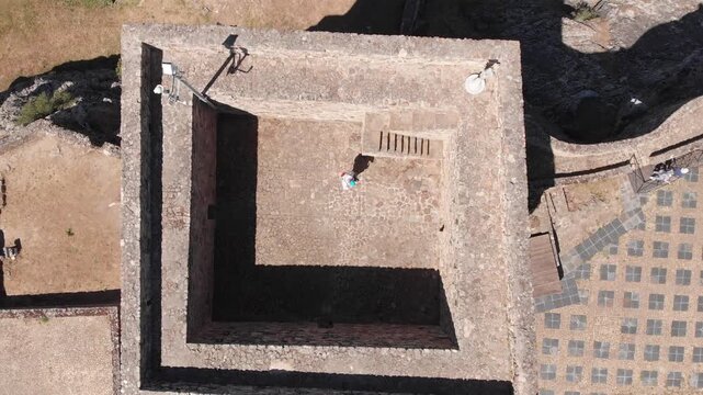 Aerial drone shot looking straight down at a tower. The drone steadily ascends vertically, gradually pulling away from the tower and revealing a wider perspective of the surrounding landscape. Marv&atilde;o