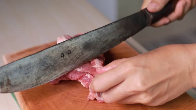 Hands chopping raw pork bone on a wooden cutting board