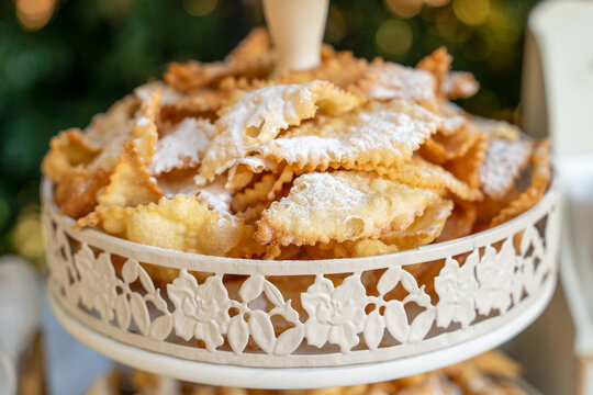 Crispy fried chiacchiere pastries dusted with powdered sugar are piled on a decorative white cake stand, a traditional carnival dessert.