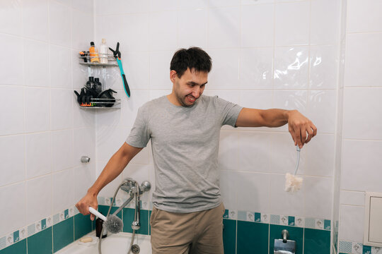 Concept of household chores and cleaning. Man finds humor, disgust in task of scrubbing toilet. Unpleasant but necessary domestic duty. Everyday life and hygiene concept