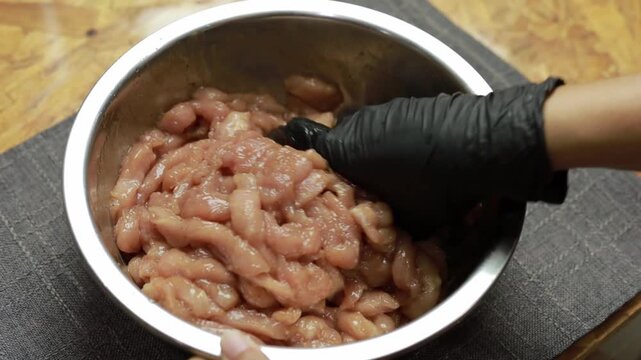 Gloved hands mixing raw sliced pork with marinade in a bowl