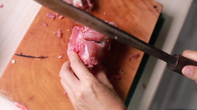 Hands chopping raw pork bone on a wooden cutting board