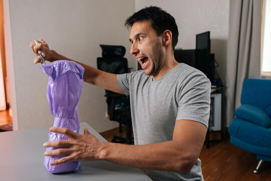 Cheerful funny customer male struggling with impossible to open consumer product. Concept of wrap rage, bad packaging design, customer dissatisfaction. Man in casual clothes at desk