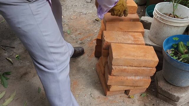 Young man arranging and aligning clay red bricks outdoors