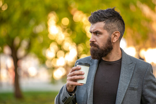 Handsome man on street holding cup of coffee. Business lifestyle, break. Man drinking morning coffee. Coffee break in fall outdoor. Bearded man having coffee in autumn street. Seasonal drink