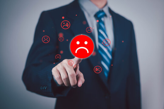 Businessman touching a digital sad face icon, symbolizing customer dissatisfaction, negative feedback, poor service, complaints, and declining business reputation.