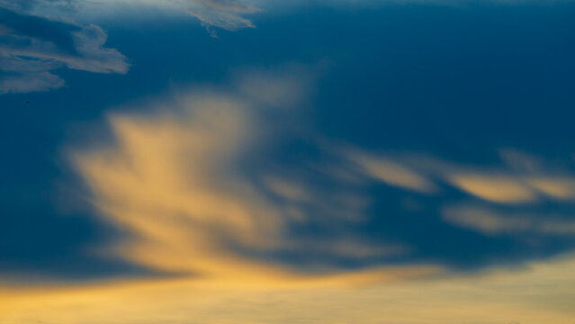 Beautiful golden hour sunset clouds in a deep blue sky.A stunning abstract long-exposure style photograph capturing soft, wispy clouds glowing with warm golden and yellow light during twilight .