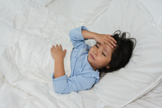 sick preschoool child girl touching her forehead with fever headache in bed