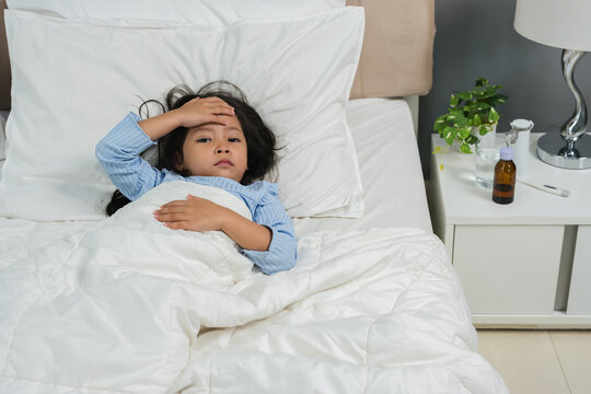 sick preschoool child girl touching her forehead with fever headache in bed