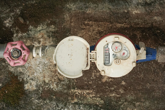 Close-up of a Water Meter with Valve on Rusty Pipe