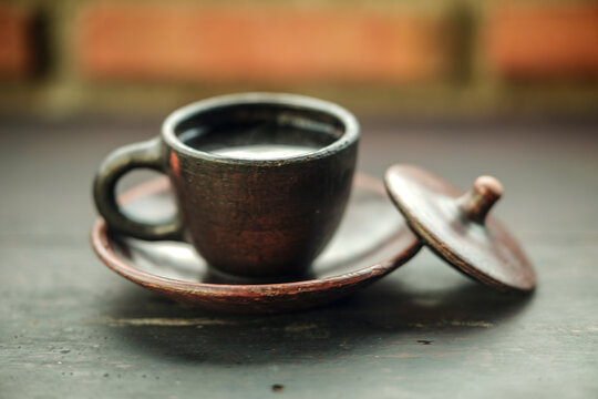 Traditional clay coffee cup with saucer and lid on a dark wooden table with blurred brick background
