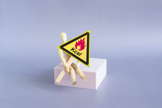 The warning sign &ldquo;Dangerous Calories&rdquo; in the form of a yellow triangle on a stand in the hands of a doll. The concept of &ldquo;dangerous calories&rdquo;.