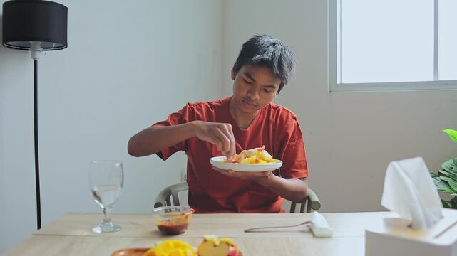 Young Asian man pouring spicy paste to plate and Enjoy eating sliced fruit from plate at table