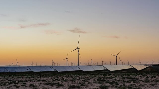 Solar photovoltaic panels at sunrise/sunset; wind turbine power plant; new energy