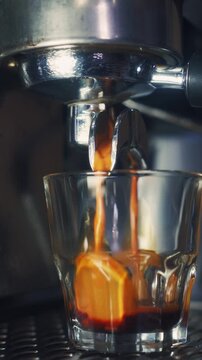 Fresh hot espresso pouring into a clear glass tumbler on an espresso machine drip tray. Beautiful golden cream and rich flow for cafe and breakfast b-roll