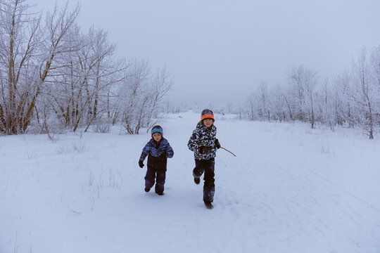 Two boys running in a snowy field on a cold winter day