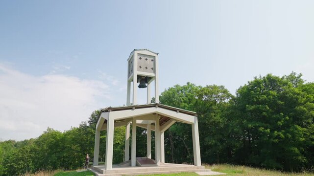 Skamlingsbanken bell tower and memorial pavilion on a grassy hill in Denmark, a historic national gathering place surrounded by woodland under a bright summer sky.