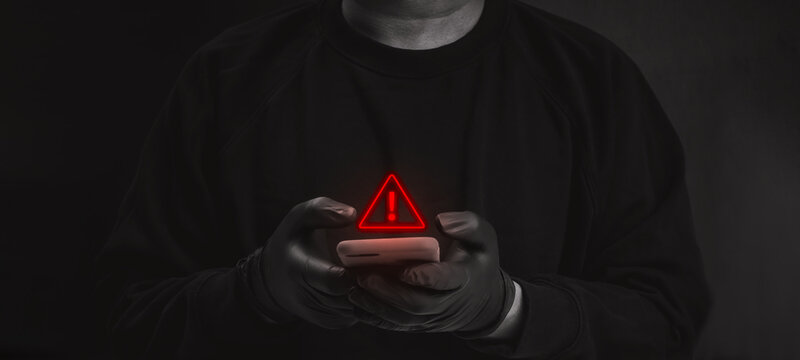 Anonymous scammer person uses smartphone beneath red warning alert. Mobile account takeover, unauthorized access, phishing risk, banking fraud, online scam, and digital security threats concept.