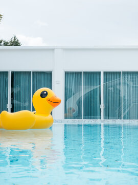 Large yellow inflatable duck floats in a clear blue swimming pool at modern party resort, creating playful summer vacation scene for travel, hospitality, leisure and family-friendly tourism campaigns.