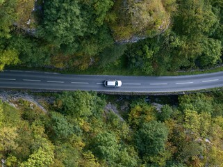 Fototapeta premium Aerial view of a white car on a winding road through a forest