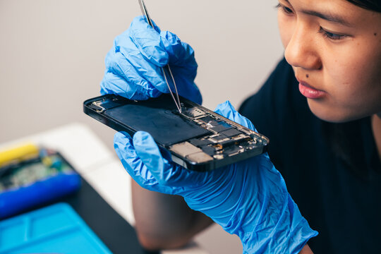 Female technician replaces smartphone lithium battery for hardware repair concept. Conceptual backdrop for phone repair service, right to repair microelectronics, and green circular economy 