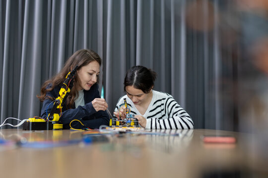 Two female students concentrate on building robotic mechanical project at wooden table during science class feeling curious and happy