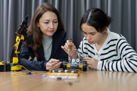 Mother and daughter building robot car together with focused expression, concentrating on assembling electronic parts for science project at home