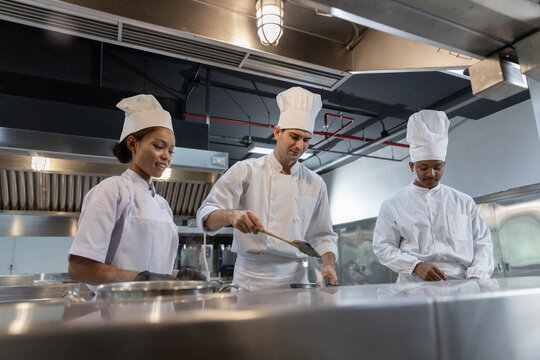 professional chef team working together in modern commercial kitchen wearing white uniform cooking food with serious expression